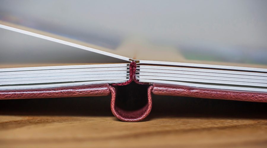 Handmade photobook with thick plastic sheets open 180 degrees, side view. Close-up of the spine of a book. Book binding